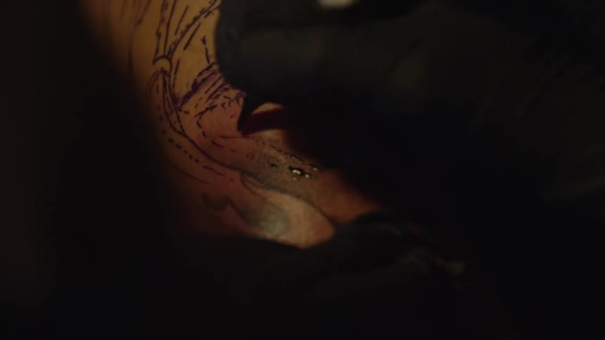 Close-up of a tattoo artist using a tattoo gun to ink a portrait design onto a person's skin