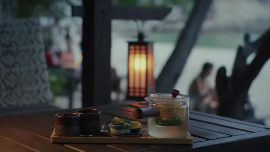 A freshly brewed pot of mint tea sits on a wooden table at a beachside cafe in the evening