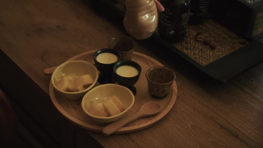 A woman pours a refreshing welcome drink into a cup on a wooden tray with fruit and yogurt at a luxury spa