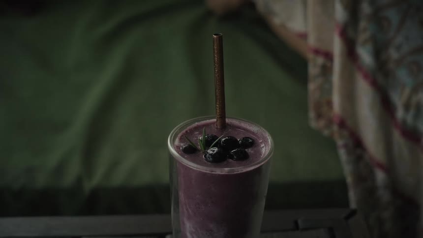 A person's hand slowly picks up a healthy purple blueberry smoothie garnished with fresh berries from a table