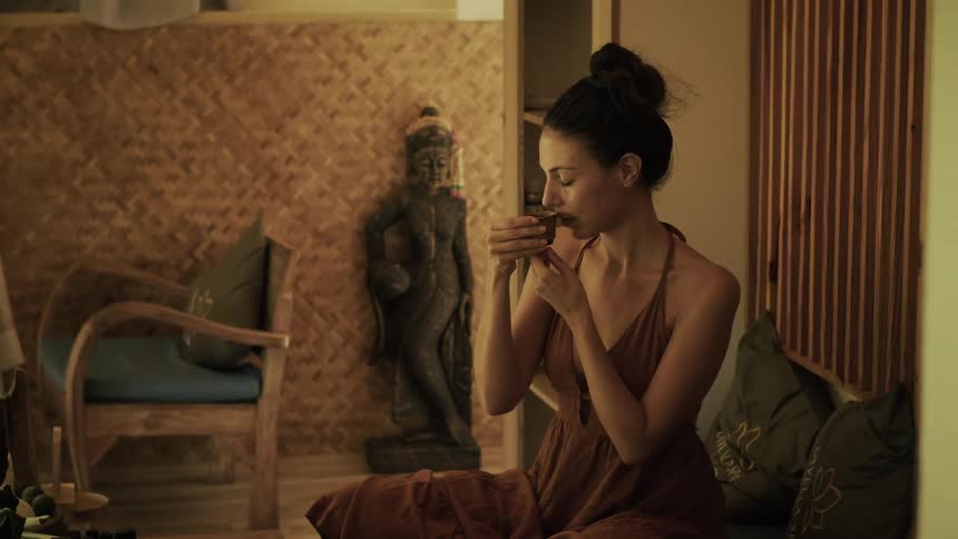 A serene woman in a flowing dress relaxes at a tranquil spa, slowly sipping a cup of traditional herbal tea