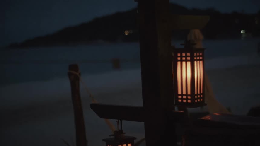 Warm lanterns gently glow on a tranquil tropical beach at night