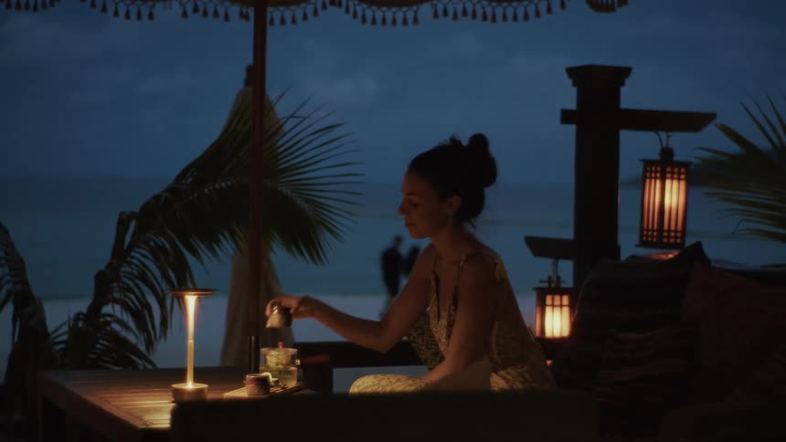 A beautiful woman enjoys a quiet and romantic evening alone at a luxurious beachfront lounge at dusk