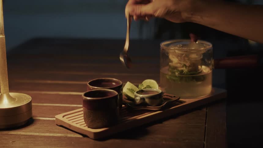 A hand squeezes a fresh lime into a ceramic teacup during a calm evening tea ceremony, shown in slow motion