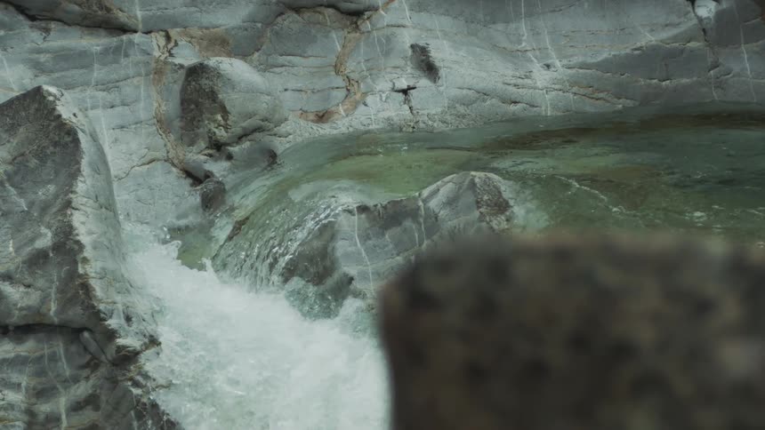 A clear stream cascades in slow motion down a rocky gorge, churning into white water