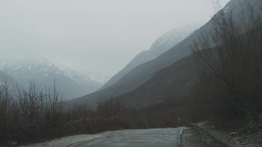 A slow drive through a moody, foggy mountain valley on a wet and overcast day, seen from a car's perspective