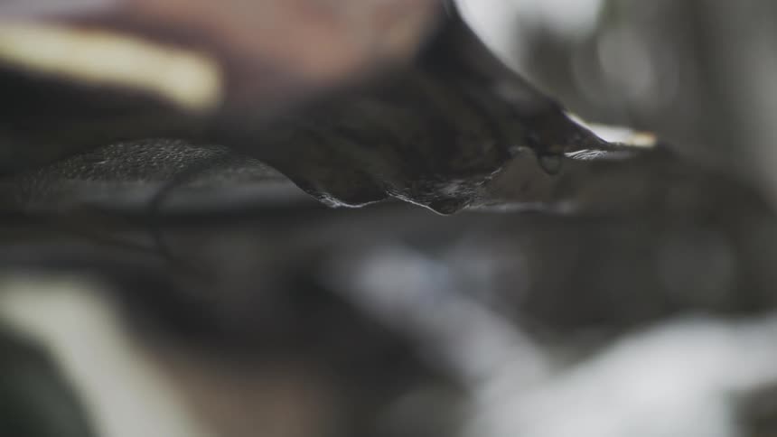 A slow-motion close-up of raindrops dripping from the edge of a rusty corrugated metal roof