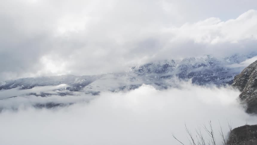 A slow panoramic view reveals a vast, snow-covered mountain landscape emerging from a thick sea of clouds