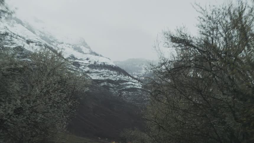 A desolate country road winds through a valley towards majestic snow-capped mountains on a gloomy, overcast day