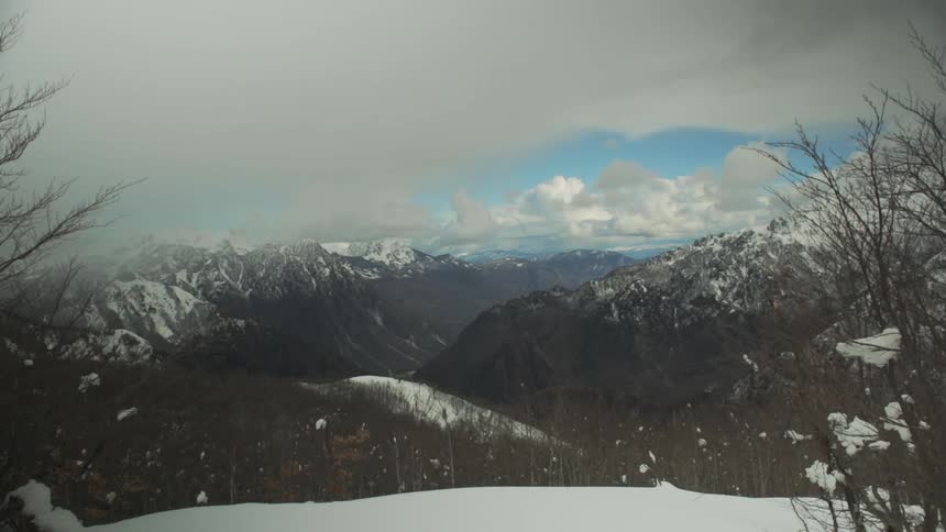 A serene wide-angle view of a snow-covered mountain range and valley under a dramatic cloudy sky during winter