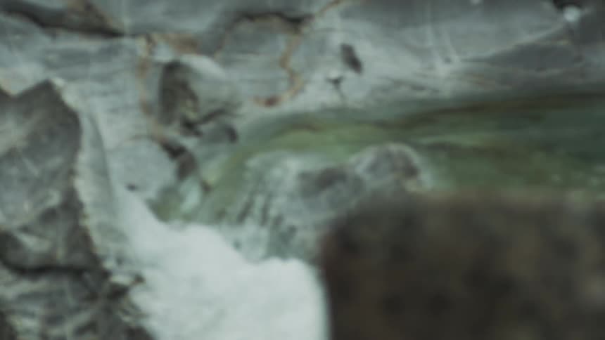 A close-up slow-motion shot of a mountain stream flowing through a rocky canyon with a gradual focus pull to a mossy rock in the foreground