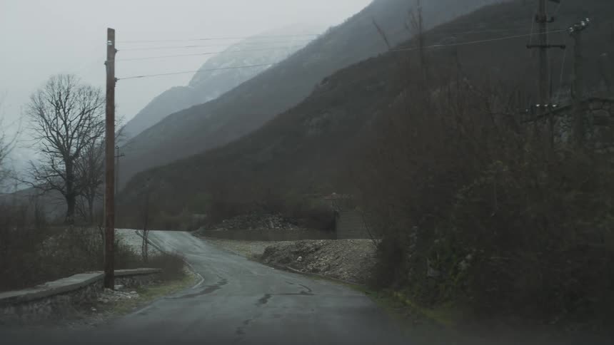 Driving slowly down a desolate, winding mountain road on a foggy and rainy day, as seen from inside a car