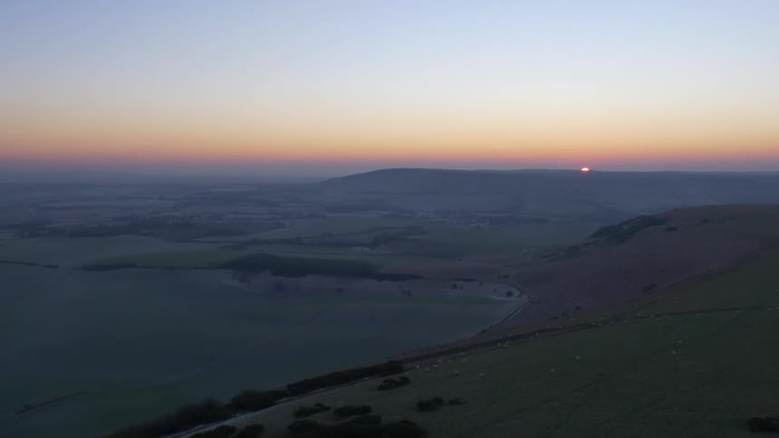 A stunning aerial view of the sun rising over the vast, rolling hills of the English countryside