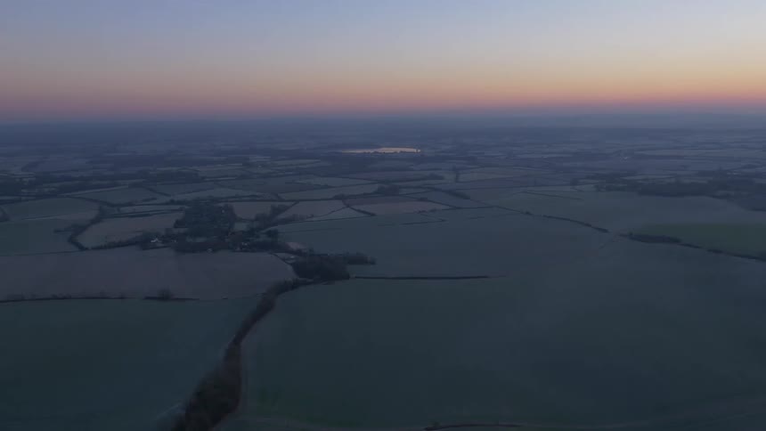 A serene aerial pan across a vast countryside landscape as the sun sets on the horizon, transitioning into twilight