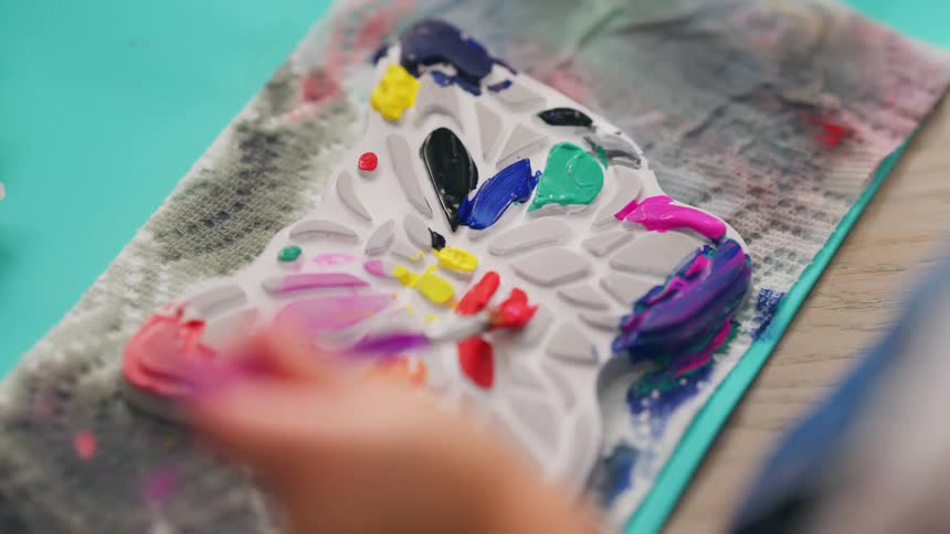 A young artist carefully adds vibrant colors to a butterfly-shaped craft project