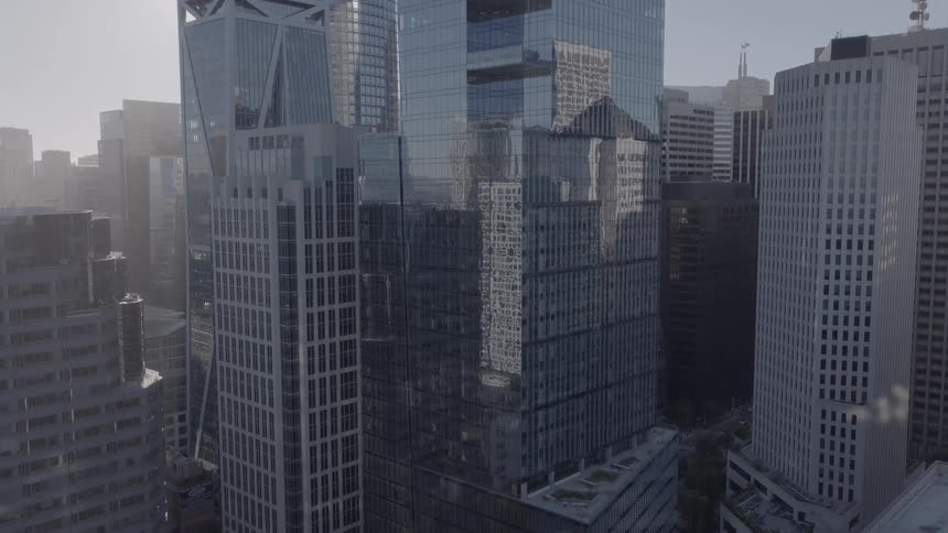 A high-angle slow tilt-up reveals the modern glass skyscrapers of a hazy downtown San Francisco financial district