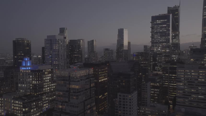 Aerial pull-back shot reveals the illuminated skyline of a modern city at dusk