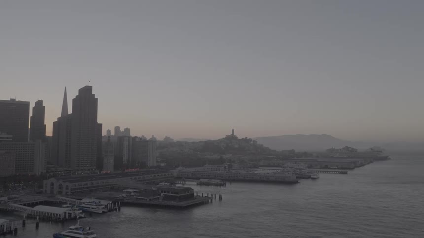 A slow aerial pull-out shot reveals the iconic San Francisco skyline and waterfront piers during a hazy sunrise
