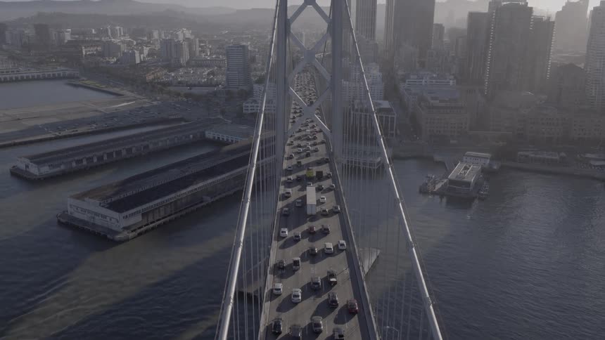 An aerial view slowly tilts up over heavy traffic on the San Francisco-Oakland Bay Bridge with the city skyline in the background