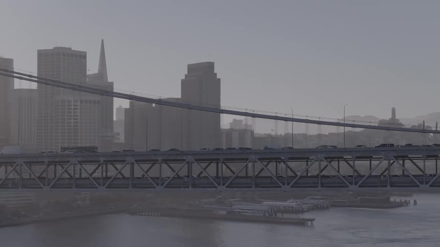 Steady traffic crosses the San Francisco Bay Bridge with the hazy city skyline in the background