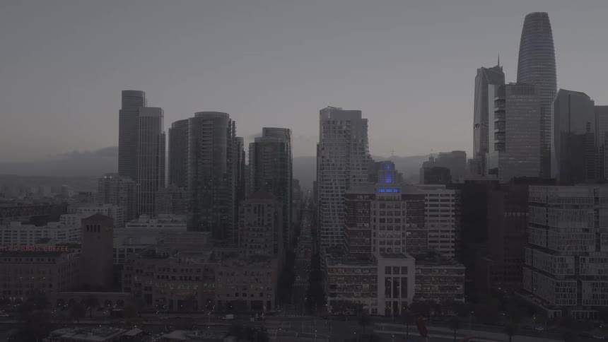 An aerial shot slowly pulls back from the towering skyscrapers of downtown San Francisco to reveal the waterfront and bay at dusk