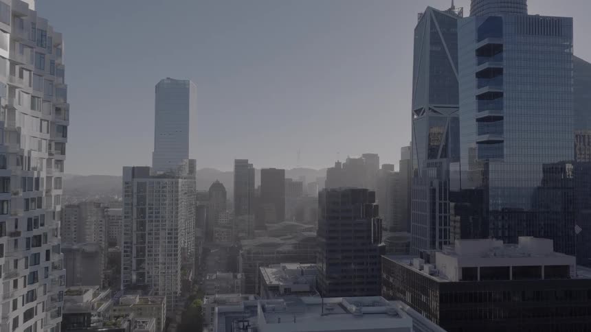 Aerial view pushes forward through a hazy downtown city skyline filled with skyscrapers as the sun shines brightly