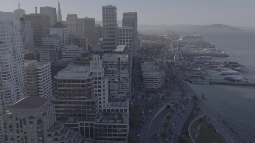 A slow aerial reveal of the San Francisco skyline and Embarcadero waterfront on a hazy morning
