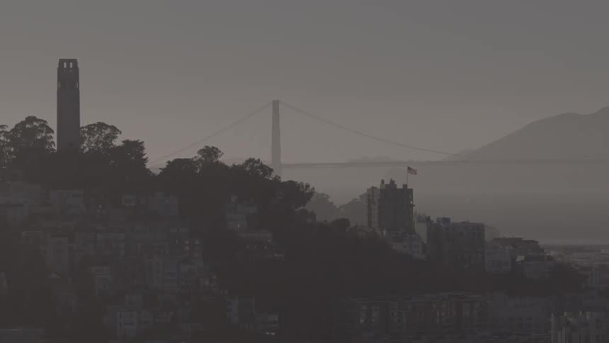 A hazy, panoramic view of the San Francisco cityscape, with a slow pan revealing Coit Tower and the Golden Gate Bridge in the distance