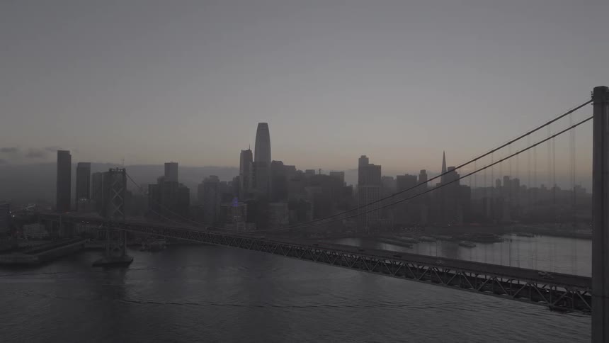 A slow aerial push-in reveals the iconic San Francisco skyline and the Bay Bridge on a foggy, overcast morning