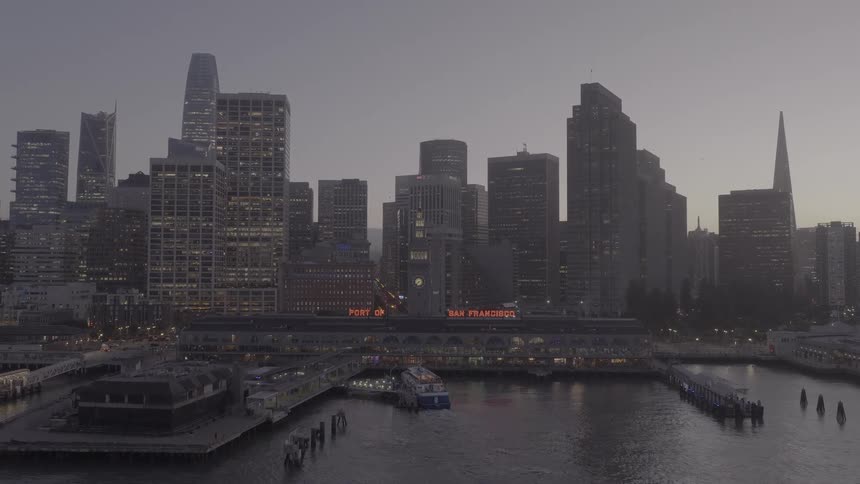 A slow aerial push-in reveals the iconic Port of San Francisco and Ferry Building against the glowing downtown skyline at dusk