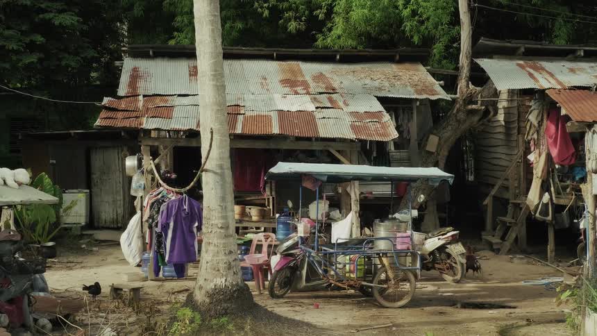 A slow zoom out from a rustic dwelling in a poor rural Asian village, featuring tin roof shacks and a motorcycle sidecar