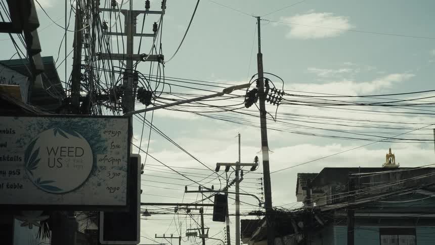 Low angle tilt down revealing a chaotic mess of overhead power lines on a street in a Thai town
