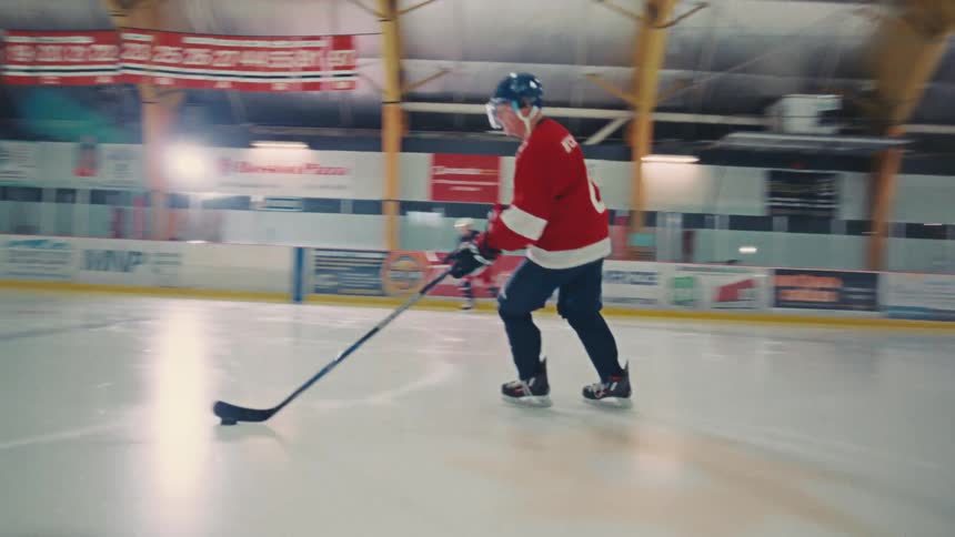 A hockey player in a red jersey stickhandles the puck while skating across the ice during practice in an arena