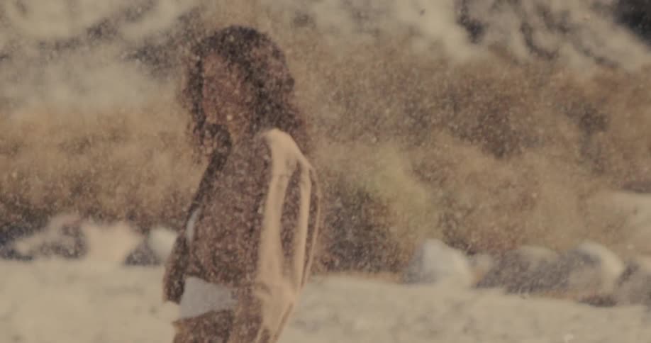 Super slow-motion shot of sand swirling in the wind, revealing a contemplative woman in the desert