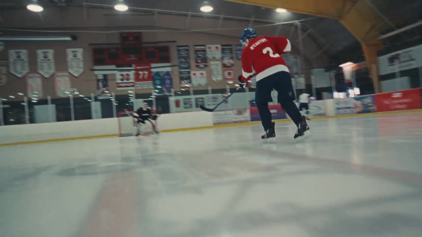 Low angle slow motion shot of an ice hockey player skating with a puck and shooting on the goalie during practice