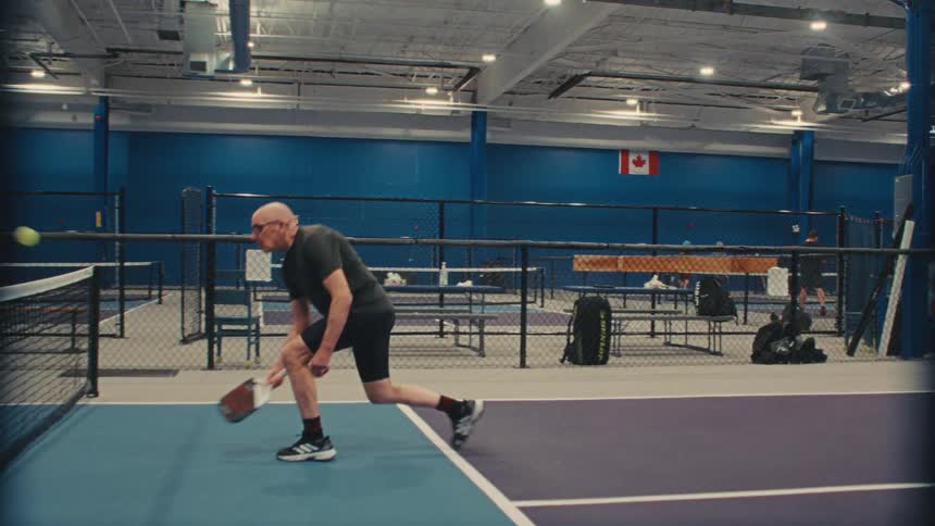 An active senior man returns a shot during a pickleball match, captured in dramatic slow motion