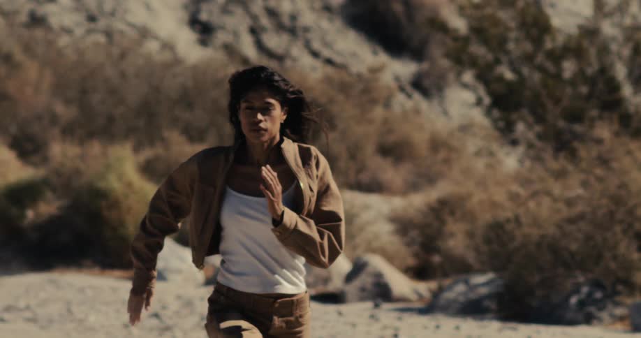 A determined woman runs in slow motion through a swarm of desert flies, with the focus shifting from her to the insects