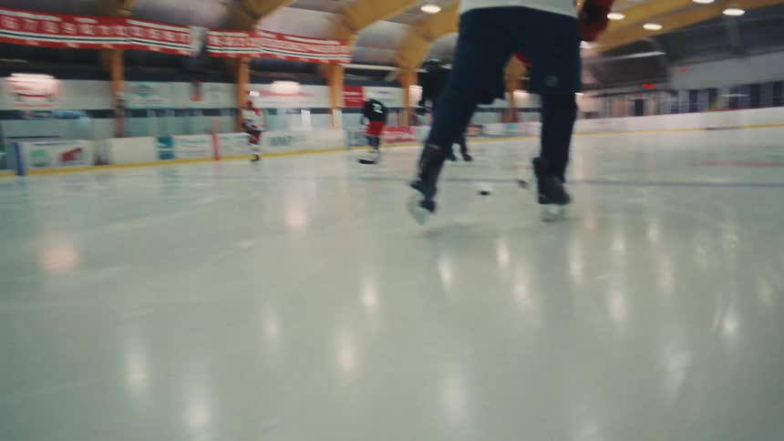 Slow-motion tracking shot follows a hockey player from behind as they skate down the ice rink while dribbling a puck