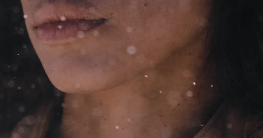 Dust particles dance in the warm light in front of a woman's stoic face in a slow-motion cinematic shot
