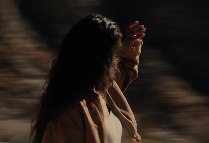 A woman stands in a desert canyon shielding her eyes from the sun as the camera rapidly pans past, creating a motion blur effect