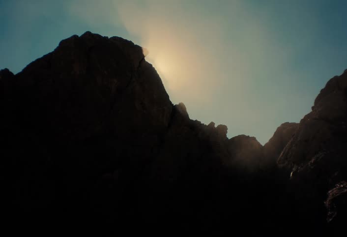 The sun moves behind a silhouetted mountain peak, creating a dramatic timelapse with lens flare and sun rays