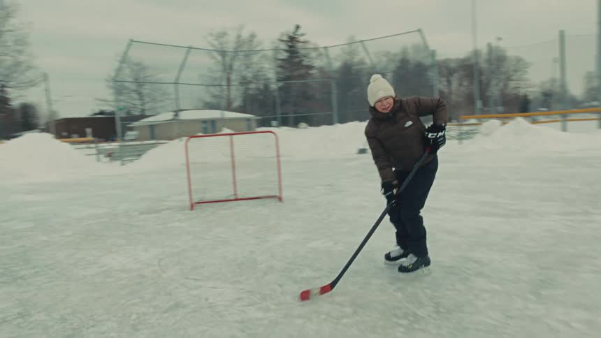 A woman stickhandles a hockey puck while ice skating on an outdoor rink in slow motion