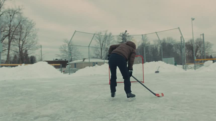 Slow motion shot of a person playing hockey, skating across an outdoor rink and scoring a goal