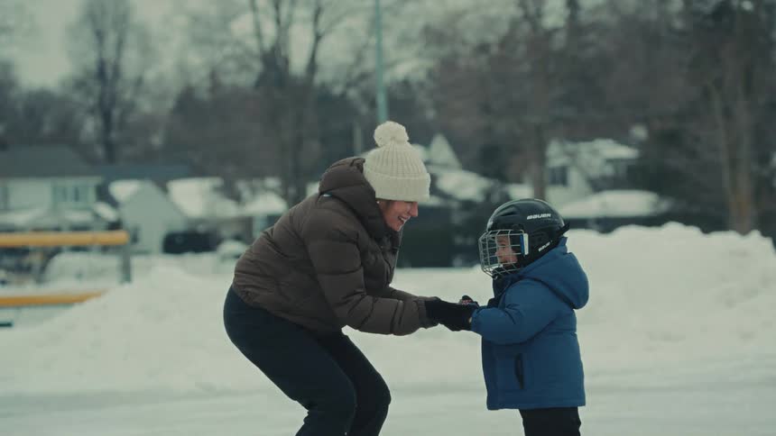 A heartwarming moment as a mother holds her young son's hands, teaching him how to ice skate on a snowy outdoor rink