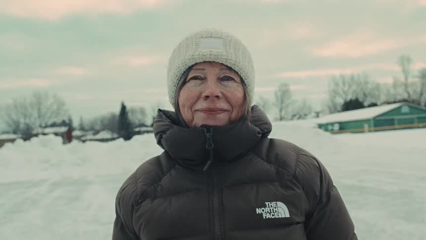 Portrait of a smiling senior woman bundled up in a winter jacket and beanie, standing outside in the snow