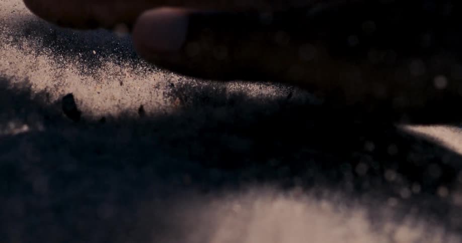 Slow motion close up of a hand gently touching the surface of warm sand