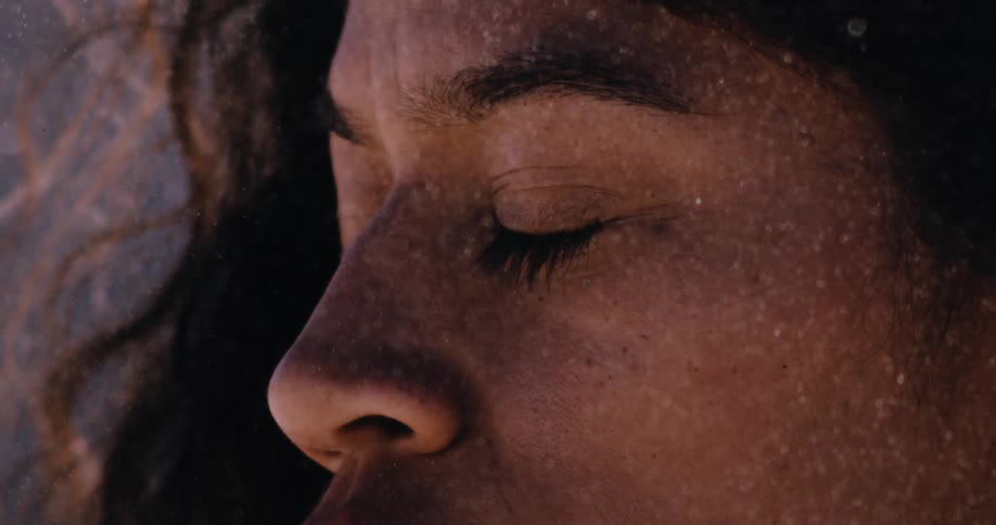 An artistic close-up captures a serene woman with her eyes closed as soft, white particles gently fall and dust her face