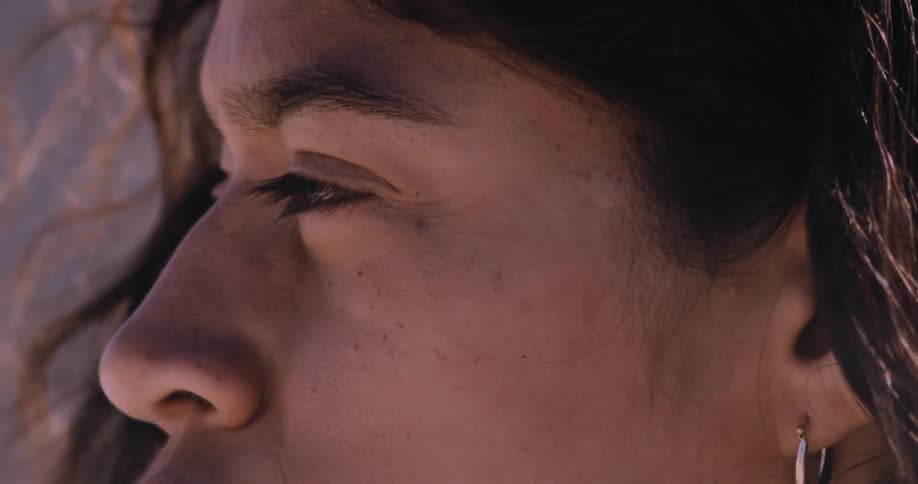 Extreme close-up of a contemplative indigenous woman's face as dust particles blow in the wind across her skin