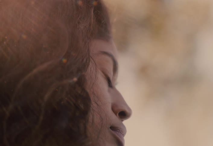 Dreamlike double exposure of a contemplative woman's face and a bright, warm light leak effect during golden hour