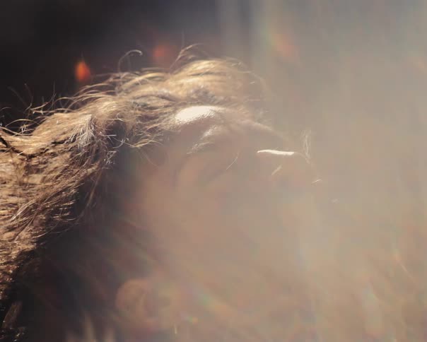 Ethereal close-up of a woman's face as she looks up and is bathed in a brilliant, warm lens flare